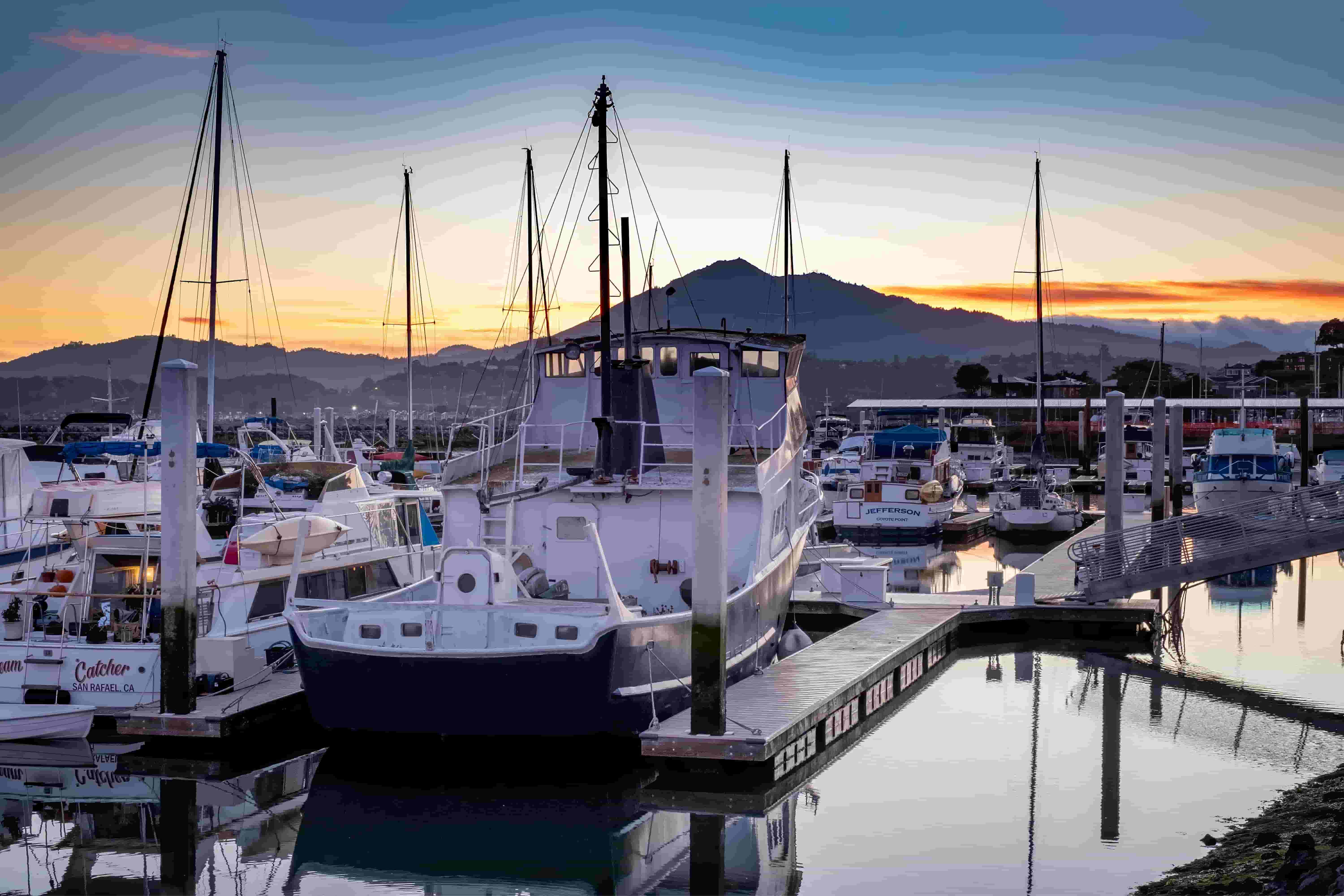 Boats docked in a marina at sunset with mountains in the background