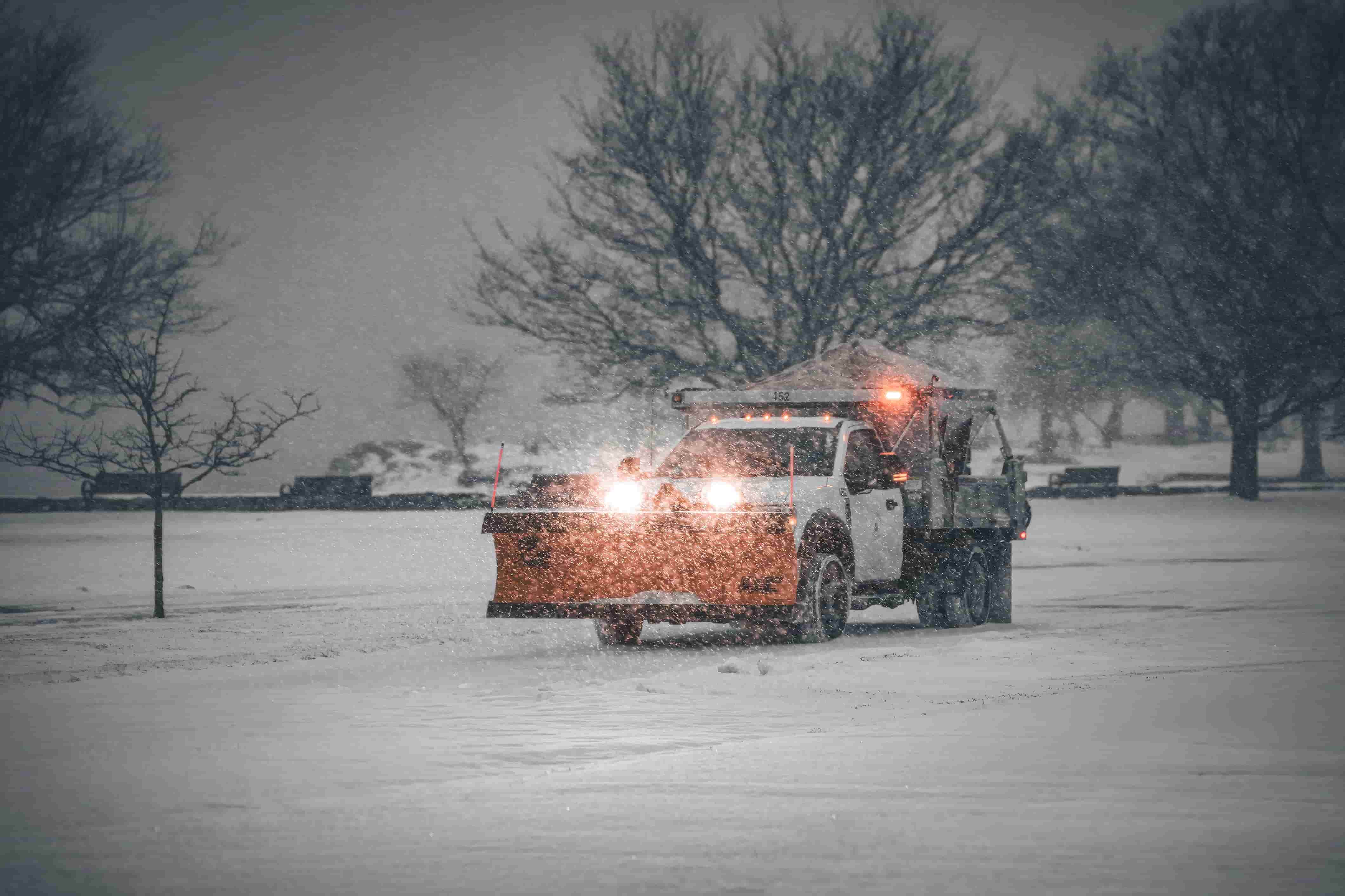 Pickup truck with an orange plow and salt spreader clearing snow during a storm