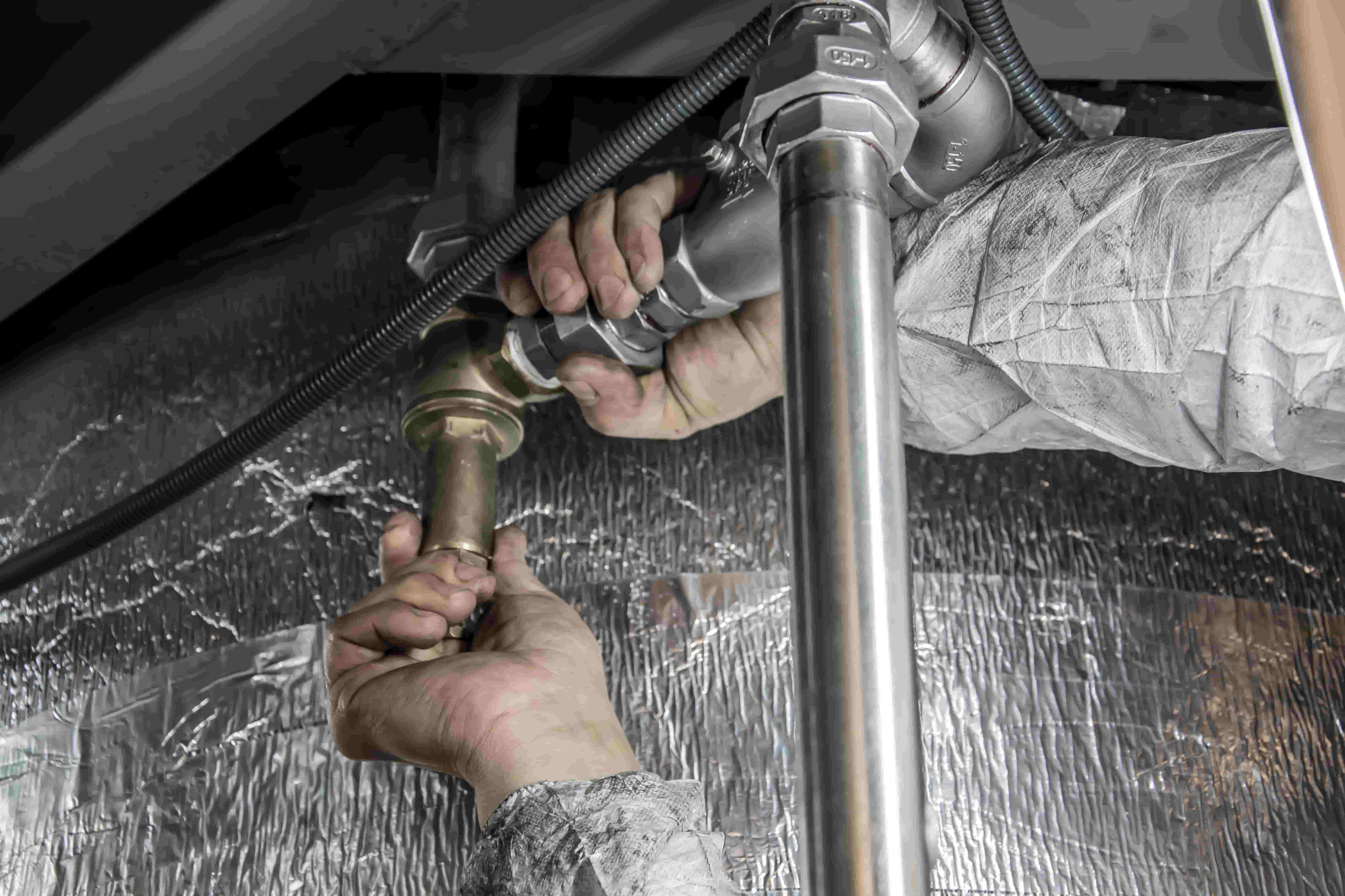 Plumber tightening a brass fitting on the pipes under a sink