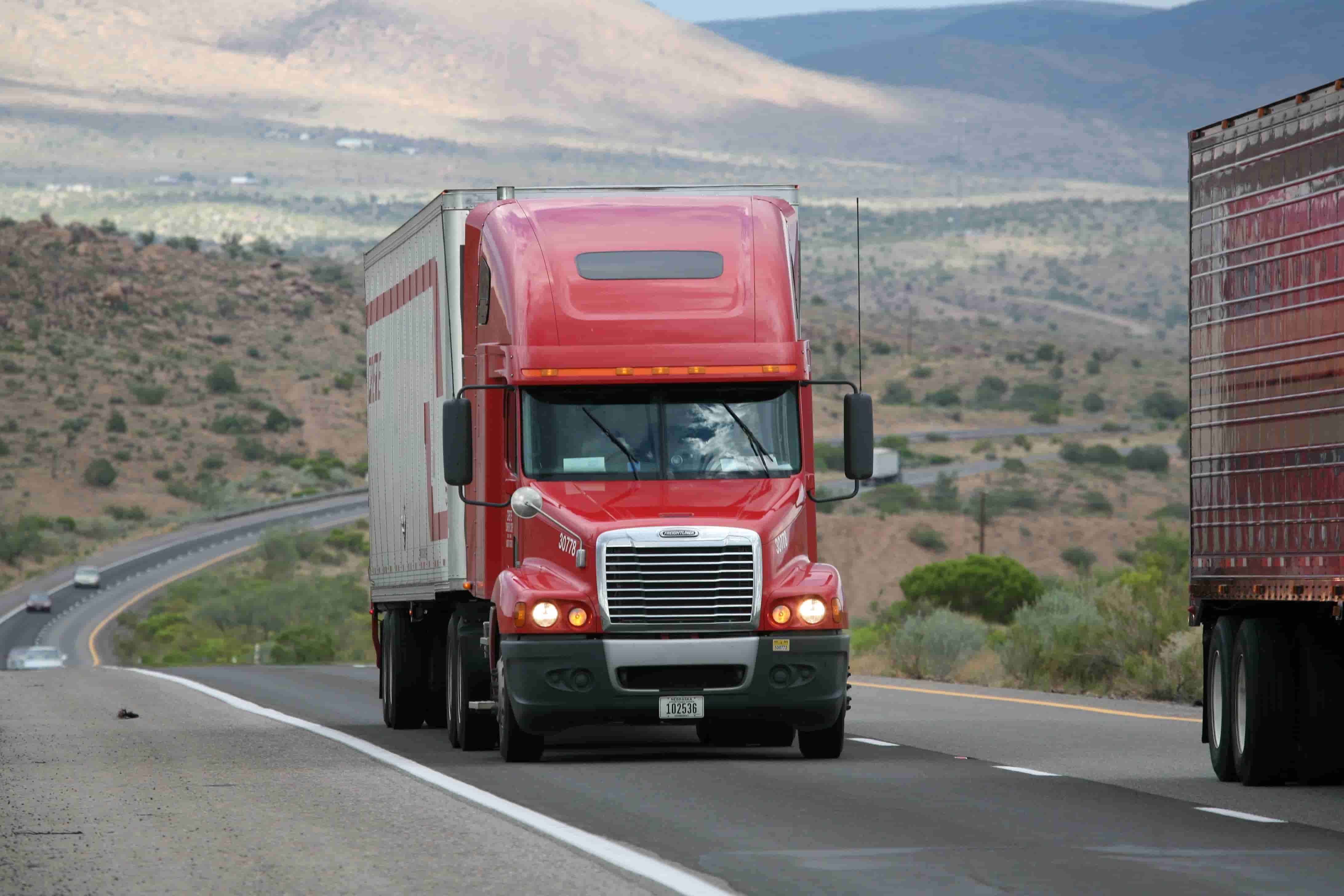 Red semi truck hauling freight on an interstate highway between states