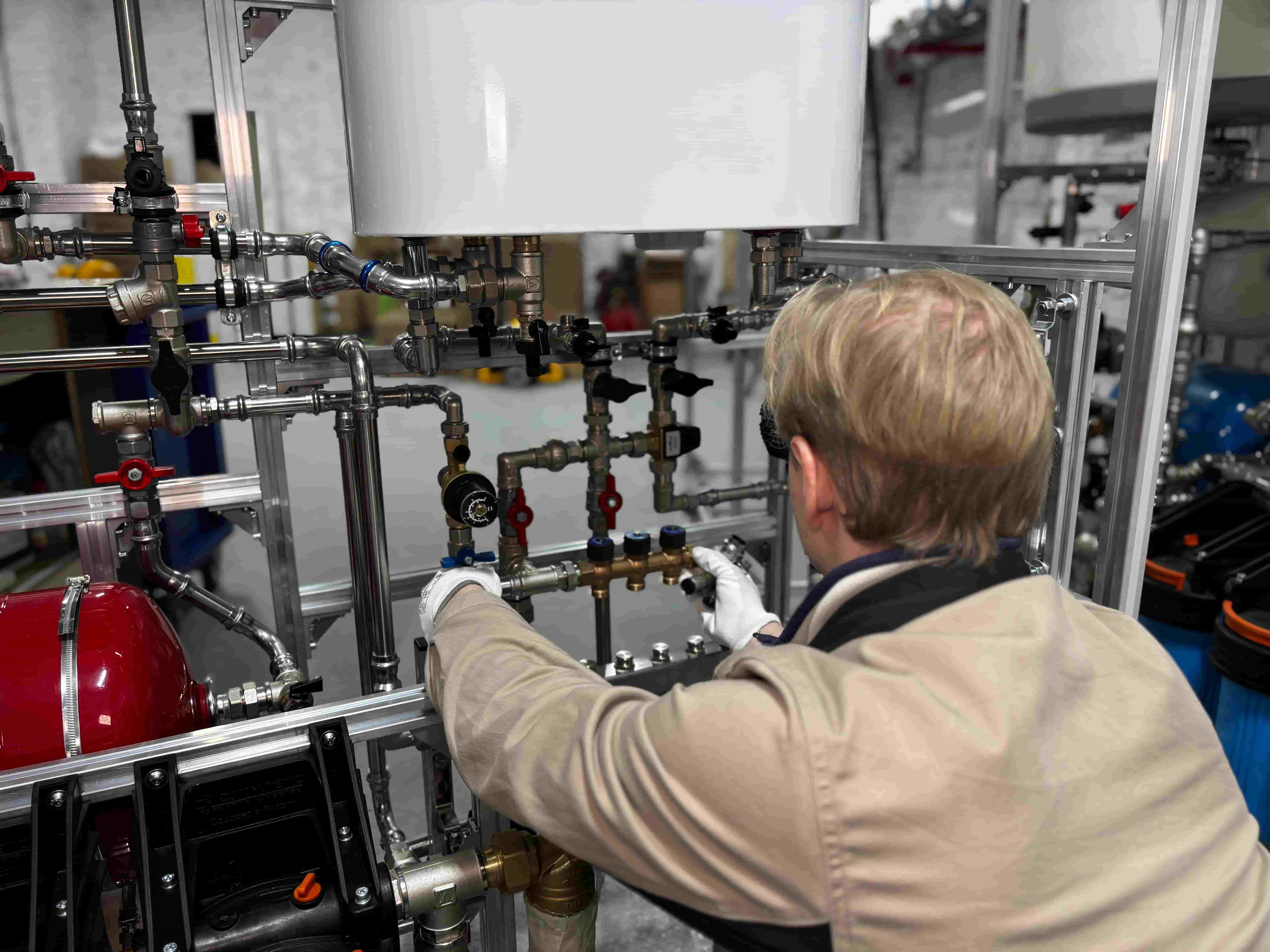 Plumber in work gloves adjusting valves on a manifold of copper and steel pipes